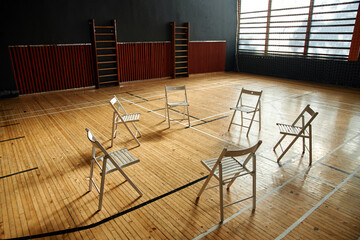 Empty circle of six chairs arranged on wooden school gym floor suggesting group therapy or psychology class setting for students with natural light streaming through large windows