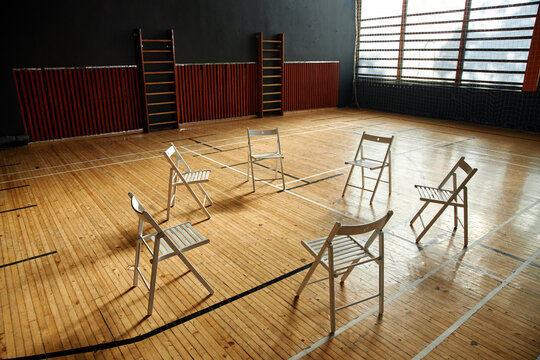 Empty circle of six chairs arranged on wooden school gym floor suggesting group therapy or psychology class setting for students with natural light streaming through large windows