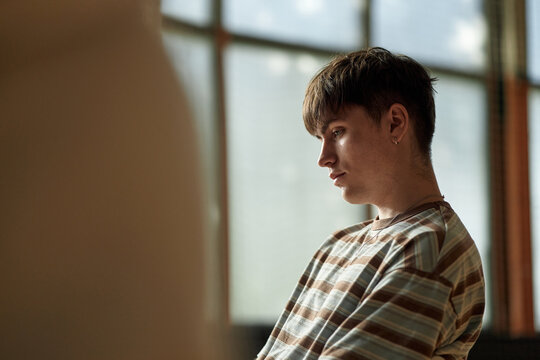 Caucasian teenage boy sitting in classroom setting looking thoughtful during psychology lesson, short brown hair visible, wearing striped shirt, large window in background