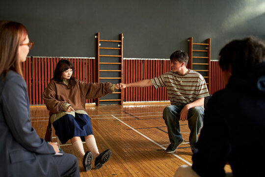 Group of multiethnic teenagers sitting in circle, Caucasian boy and Asian girl sitting opposite each other, fist bumping during psychology lesson, other students observing