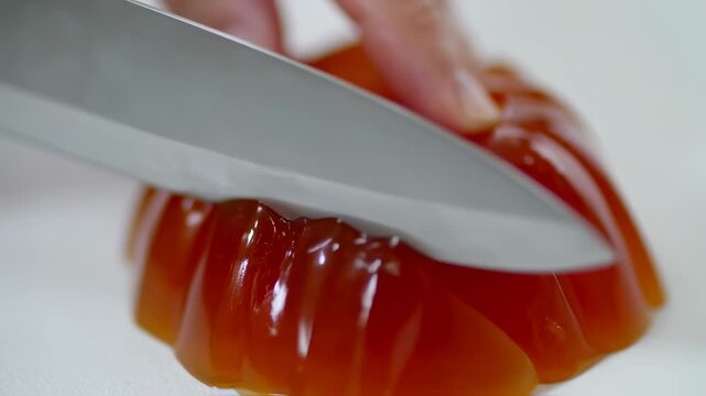 Close-up of Knife Slicing Wobbly Orange Red Gelatin Dessert