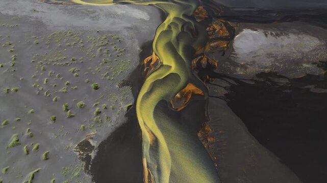 Aerial view of winding river tributaries cutting through a landscape of dark volcanic sand and vibrant green moss patches, Grindavikurbaer, Iceland.