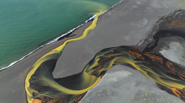 Aerial view of a river flowing into the ocean, creating a stunning contrast of yellow river water against the dark sand and turquoise ocean, Grindavikurbaer, Iceland.