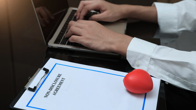 Focused new employee signing confidential NDA agreement for new job while typing on laptop with red stress heart