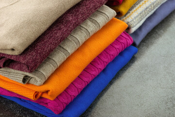 Warm clothes for fall and winter are folded in a pile. Sweatshirts, turtlenecks, and jumpers made of soft knitwear. There is space for text.