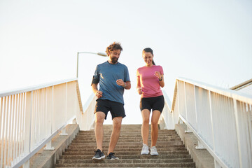 Two individuals jog down a set of stairs in a cityscape at sunset, engaging in a recreational activity that promotes health and fitness together.
