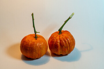 Two fresh tangerines with stems on white surface