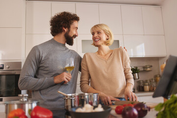Man and woman share smiles and laughter in a bright kitchen while chopping vegetables and preparing a delicious dinner together, creating a warm and inviting atmosphere.
