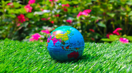 A colorful world globe placed on vibrant green grass with a blurred garden background. Small world globe on green grass with nature background