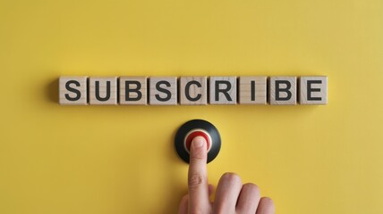 Wooden blocks spell out the word subscribe above a finger pushing a red activation button on a bright yellow background
