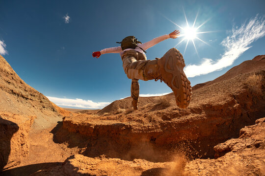 Hiker man runs and jumps across the natural gap in desert. Close up photo of hikers leg and boot while he flies