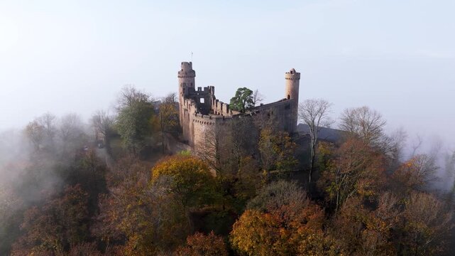 Aerial view of Burgruine Auerbach, a medieval castle ruin emerging from the autumn foliage, veiled in ethereal mist, Bensheim, Hessen, Germany.