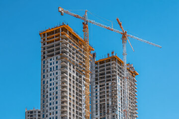 Construction of modern high-rise buildings featuring towering cranes against a clear blue sky in an urban development site