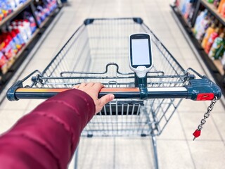 A hand-held bar code scanner on a shopping cart in a large supermarket. Modern Shopping Cart with Digital Display for Enhanced Grocery Shopping Experience and Efficient Product Selection © NBLX
