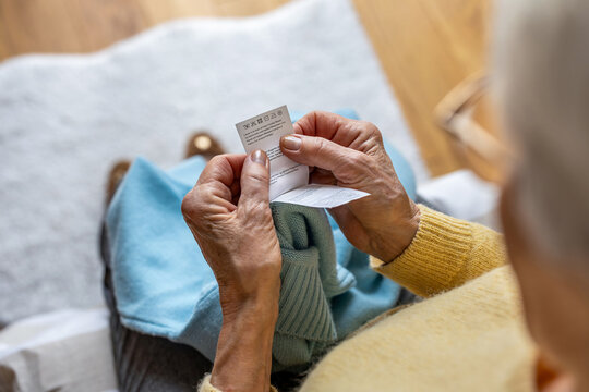 Elderly woman's hands holding a laundry label. Inscriptions in Spanish, English, German and Italian: Wash by hand with cold water, Do not use bleaching agents, Do not tumble dry, Iron at maximum 150C
