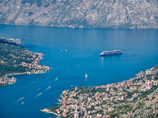 A calm view of the Bay of Kotor with a large cruise ship surrounded by mountains, blue water, and small coastal settlements. A tranquil Mediterranean landscape perfect for travel imagery.
