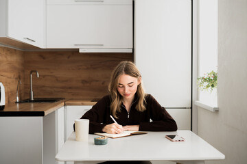 Focused young woman writing notes in notebook thoughtful and concentrated. studying, journaling at home