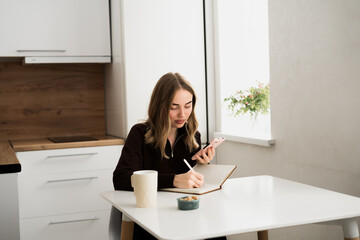 Young woman using smartphone writing notes in the notebook. doing planning and assignment.