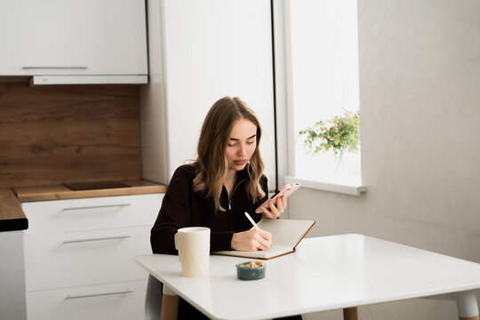 Young woman using smartphone writing notes in the notebook. doing planning and assignment.