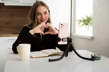 Social media live streaming concept. Female influencer blogger talking on smartphone has video blog on social network shows heart symbol at camera