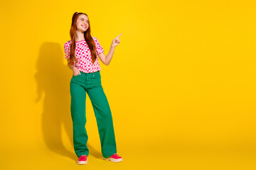 Young girl in pink checkered t shirt and green pants poses with finger point against a bright yellow background for fashion lifestyle advertising stock photo