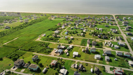 Large grid of elevated homes and open fields surround Beach Boyt, grassy vacant wetland and road network linking this low-density, flood-aware community to the Gulf coast in Port Bolivar, Texas © trongnguyen