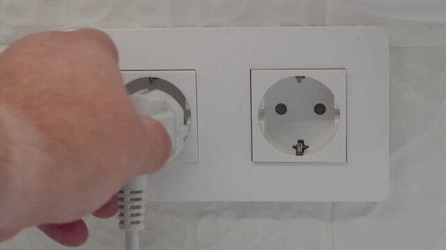 A hand inserts or removes a plastic electric plug from the wall socket. The action produces a clear, dry click as the electrical connection is made or broken.
