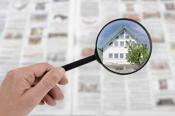 Magnifying glass highlighting house photo in newspaper, symbolizing real estate search and analysis.