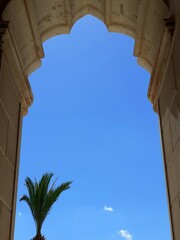 Un arco in stile gotico-moresco incornicia il cielo azzurro. Palma in primo piano.