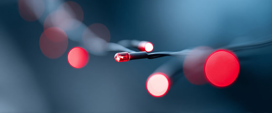 Close-up of glowing red LED lights on black wires with blurred bokeh background in cool blue tones