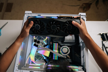 Top view of computer technician carefully inserting high-performance graphic card inside gaming desktop, upgrading powerful system with vibrant RGB lighting for maximum computing potential