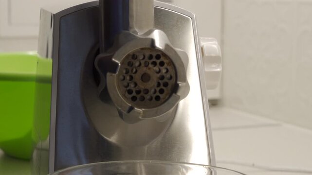 The metal electric meat grinder turns on, creating a loud, continuous, grinding and whirring sound while running idle. The noise intensifies when meat is added for processing.