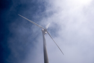 Wind turbine mast emerging through soft bright fog, viewed from below against clear sky image