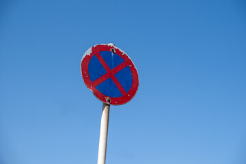 Weathered no stopping road sign stands against clear blue sky within bright daylight