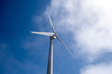 Wind turbine blades beneath bright daytime blue sky, captured from below featuring soft clouds drifting