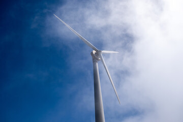 Wind turbine tower rising into soft cloudy sky, captured from below within bright daylight