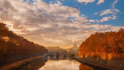 Autumn and foliage in Rome. Panoramic view of  River Tiber in mist during sunset with iconic St Peter dome and sycamore orange leaves