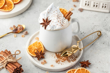 Hot cocoa drink with whipped cream, dried orange and spices in mug on white festive christmas table background