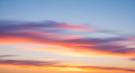 Obraz premium Soft pastel clouds glowing in pink, orange, and purple hues drift across a calm blue sky at sunrise, creating a dreamy and peaceful horizon.