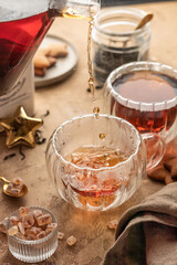 Pouring black tea into transparent glass cup from teapot on brown textured table background. Frozen spalshes of tea in cup