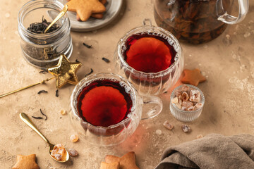 Black tea in two transparent glass cups on brown textured table background with teapot, cookies and ingredients. Cozy breakfast teatime