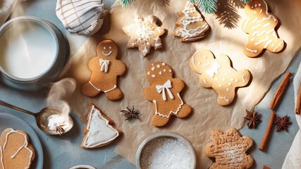 Cozy holiday baking scene featuring gingerbread cookies arranged on parchment with icing decor, warm spices, cinnamon sticks, cocoa dust, star anise, and a mug of milk nearby - Powered by Adobe