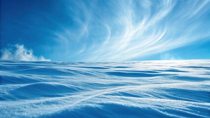 A serene winter landscape featuring smooth, undulating snow under a bright blue sky with wispy clouds.