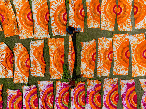 Narayanganj, Bangladesh - 19 September 2024: Aerial view of vibrant orange and pink tie-dye fabrics, laid out to dry on the grass, creating a mesmerizing pattern from above.