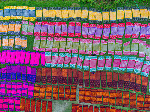 Narayanganj, Bangladesh - 10 September 2022: Aerial view of vibrant, colorful textiles spread across a grassy field, creating a rich tapestry of patterns and tones.