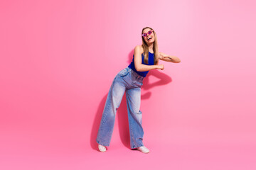 Happy young woman dancing in a pink studio wearing blue top jeans smiling in a playful fashion photo shoot