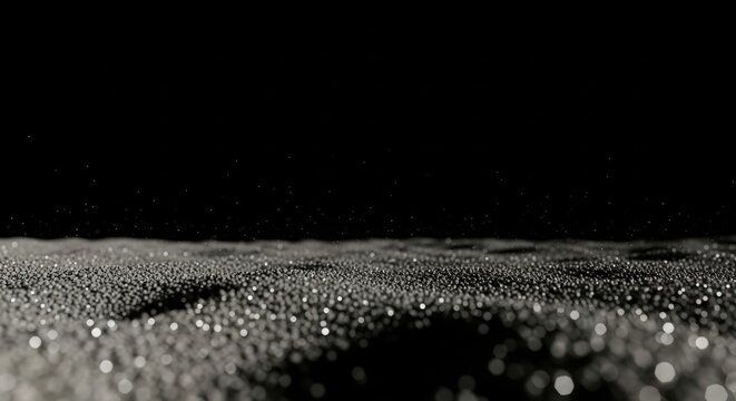 black and gray background - Low-angle close-up of a vast glittering granular surface with tiny reflective beads catching light, forming undulating dark dunes against a deep black background faintly