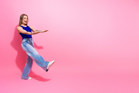 Young woman in blue top and jeans kicks with joy against pink background for casual fashion lifestyle and summer style advertising and shopping campaign - Powered by Adobe