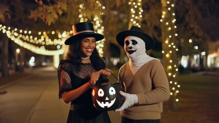 Couple in Halloween costumes with trick or treat bucket at night with string lights image photo - Powered by Adobe