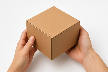 A pair of hands carefully holds a small, plain brown cardboard cube against a clean white background.